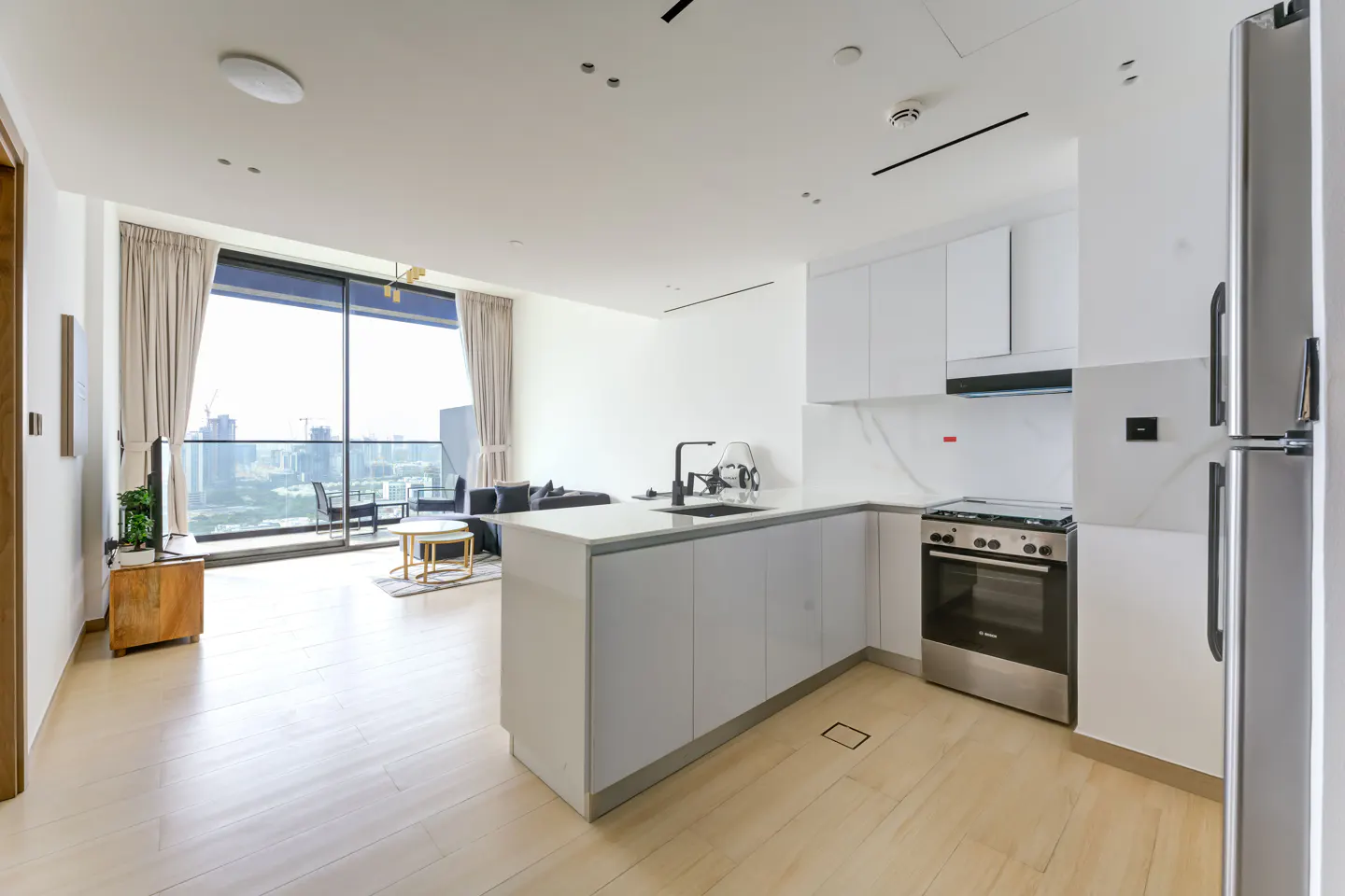 Bright, modern apartment interior with white cabinets, stainless steel appliances, and a city view from the balcony.