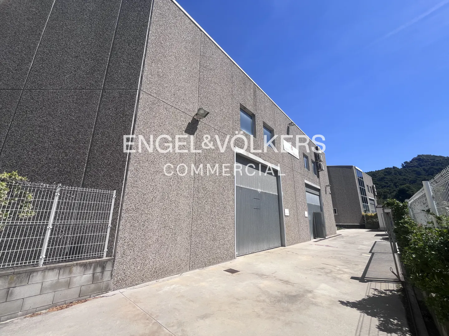 Exterior of a gray commercial building with metal doors and the Engel & Völkers logo.