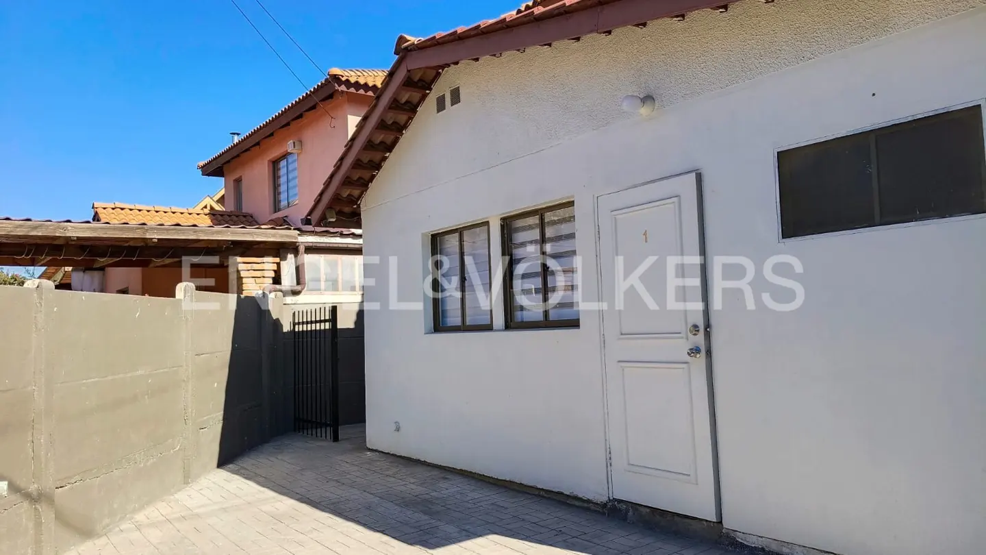 Exterior view of a white house with a red tile roof, a gray fence, and a black gate on a sunny day.