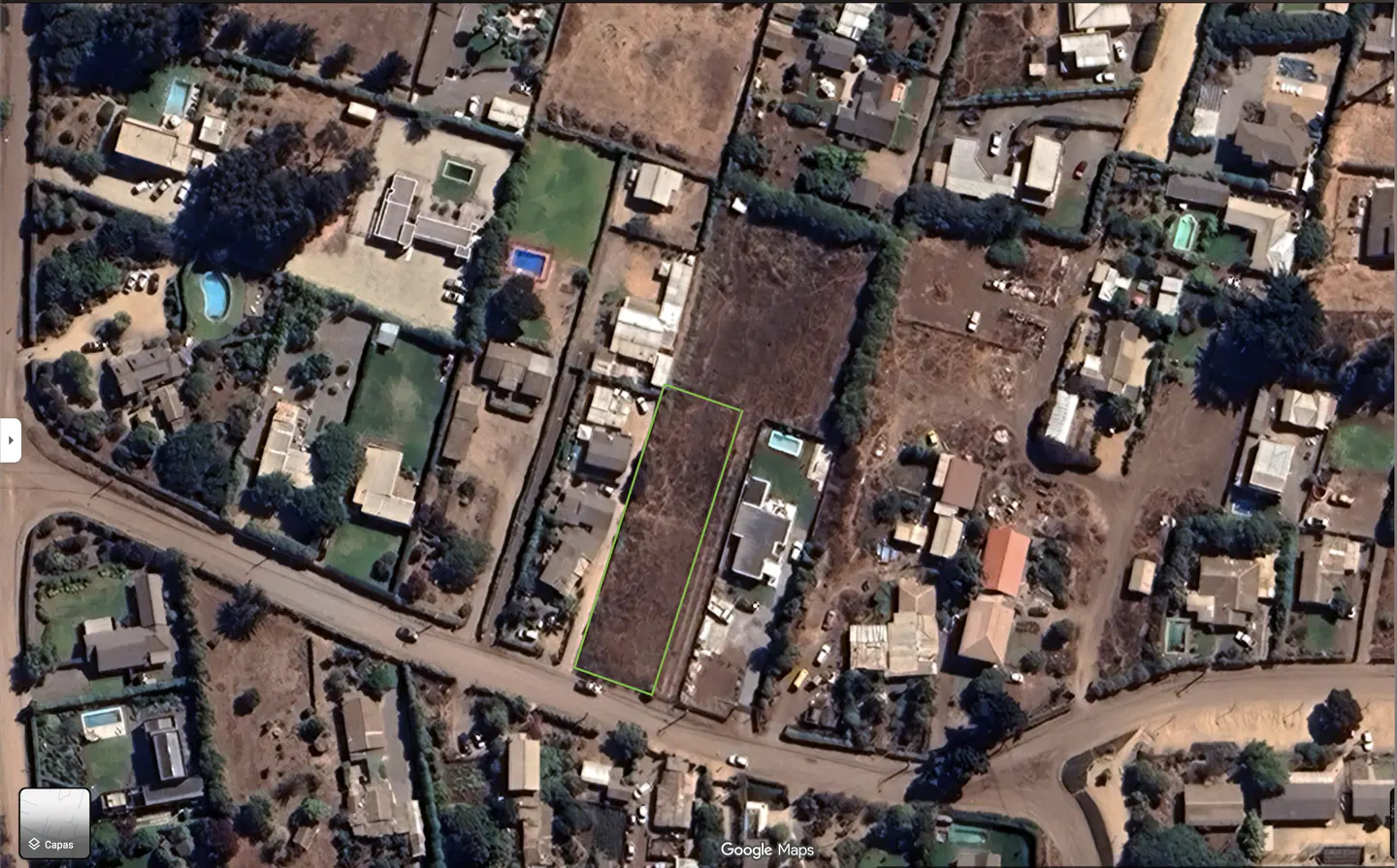 Aerial view of a rectangular vacant lot outlined in green, situated in a residential neighborhood with nearby houses.