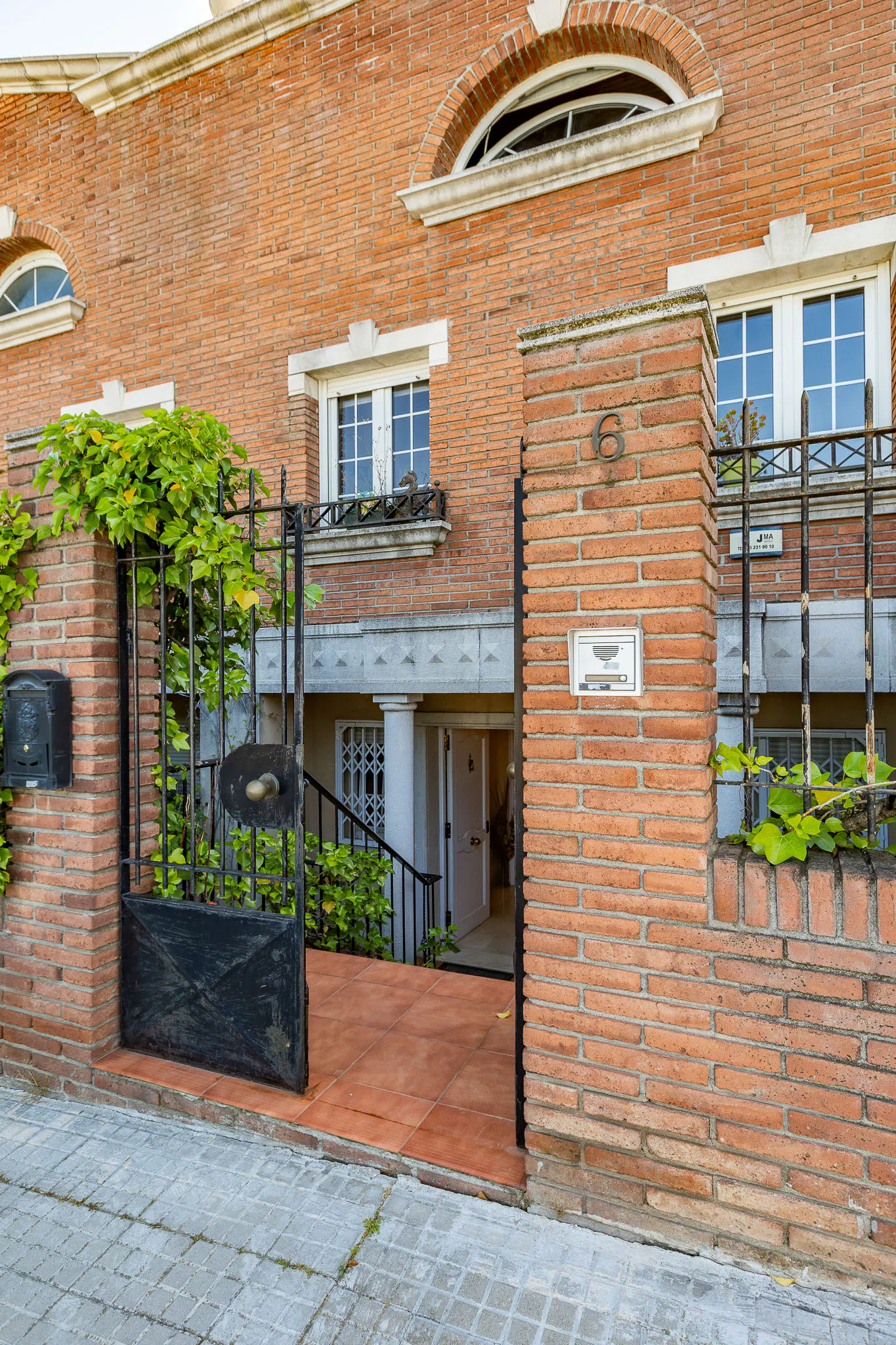 Brick house with black iron gate, green vines, and white windows. The number 6 is on the brick wall.