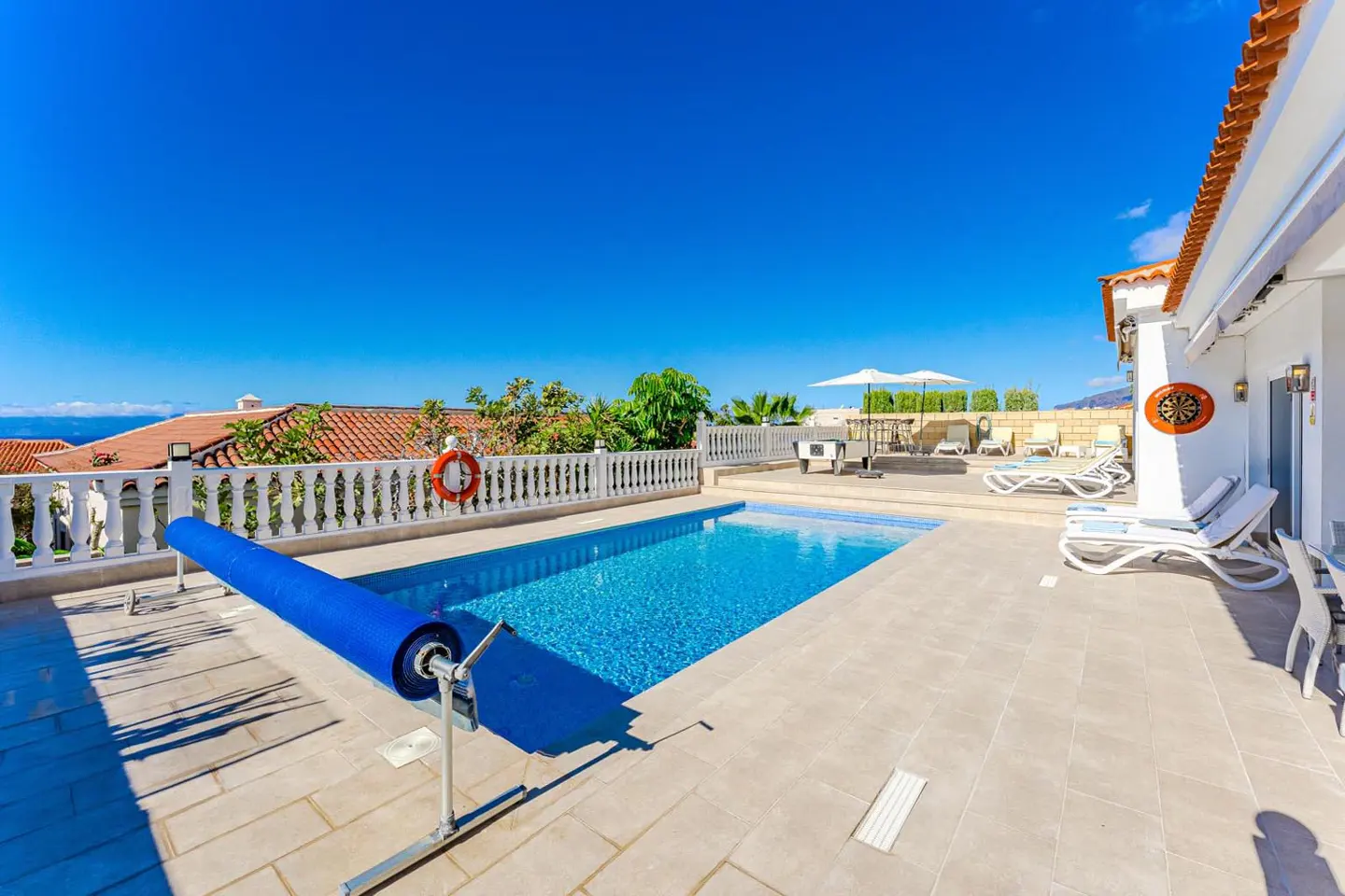 Outdoor pool with blue cover, white lounge chairs, and patio furniture under a clear blue sky.