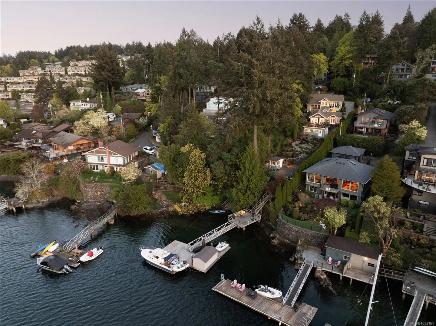 Waterfront homes with docks and boats on a tree-lined coast. Houses are nestled among green trees on a hillside overlooking the water.