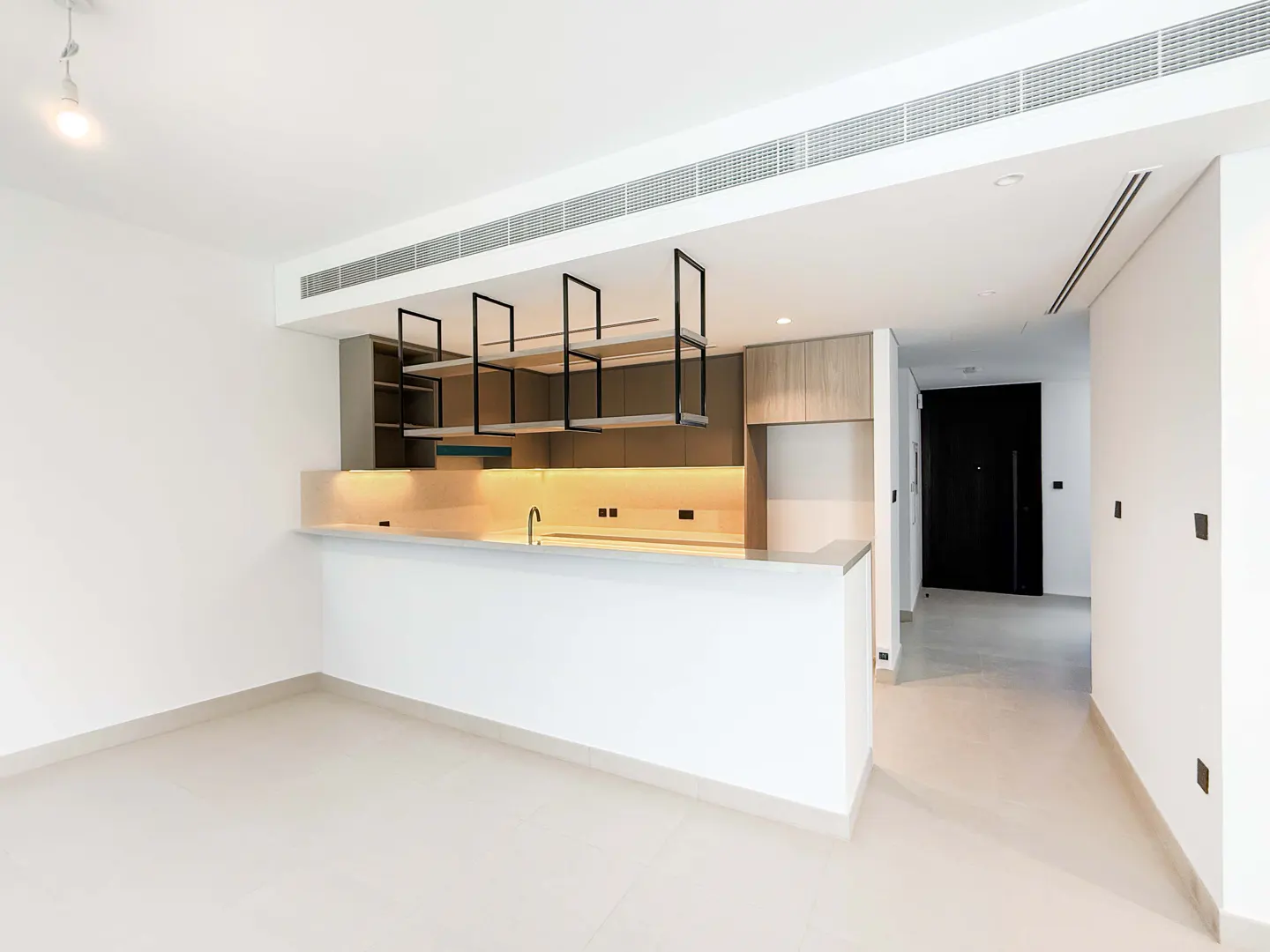Bright, modern kitchen with white walls, light tile floors, and a breakfast bar. Black shelving hangs above the counter.