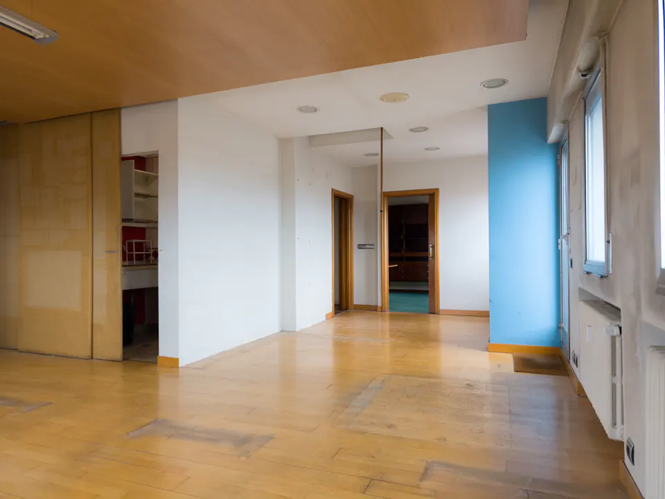 Empty room with wood floors, white walls, and a blue accent wall. There are doors leading to other rooms and windows on the right side.