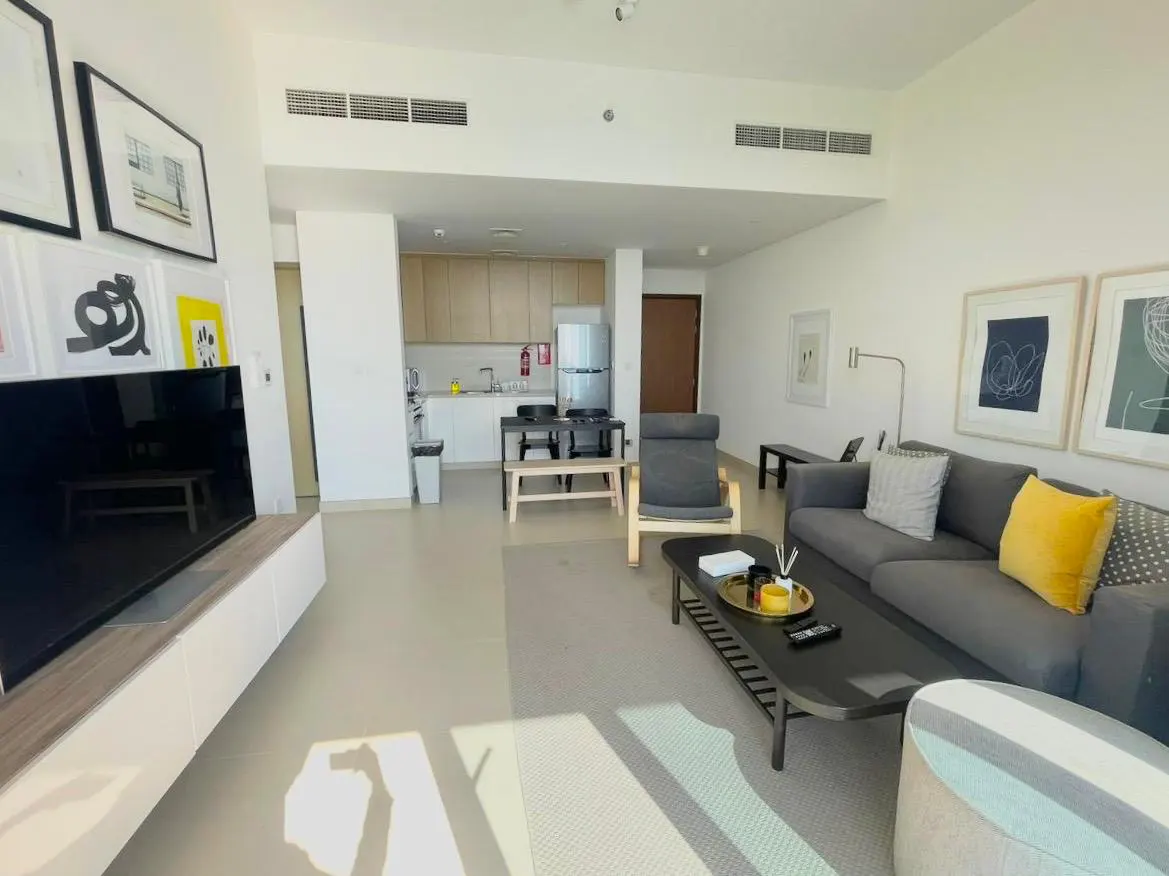 Bright, modern apartment interior with a gray sofa, black coffee table, and open kitchen. Artwork adorns the walls.