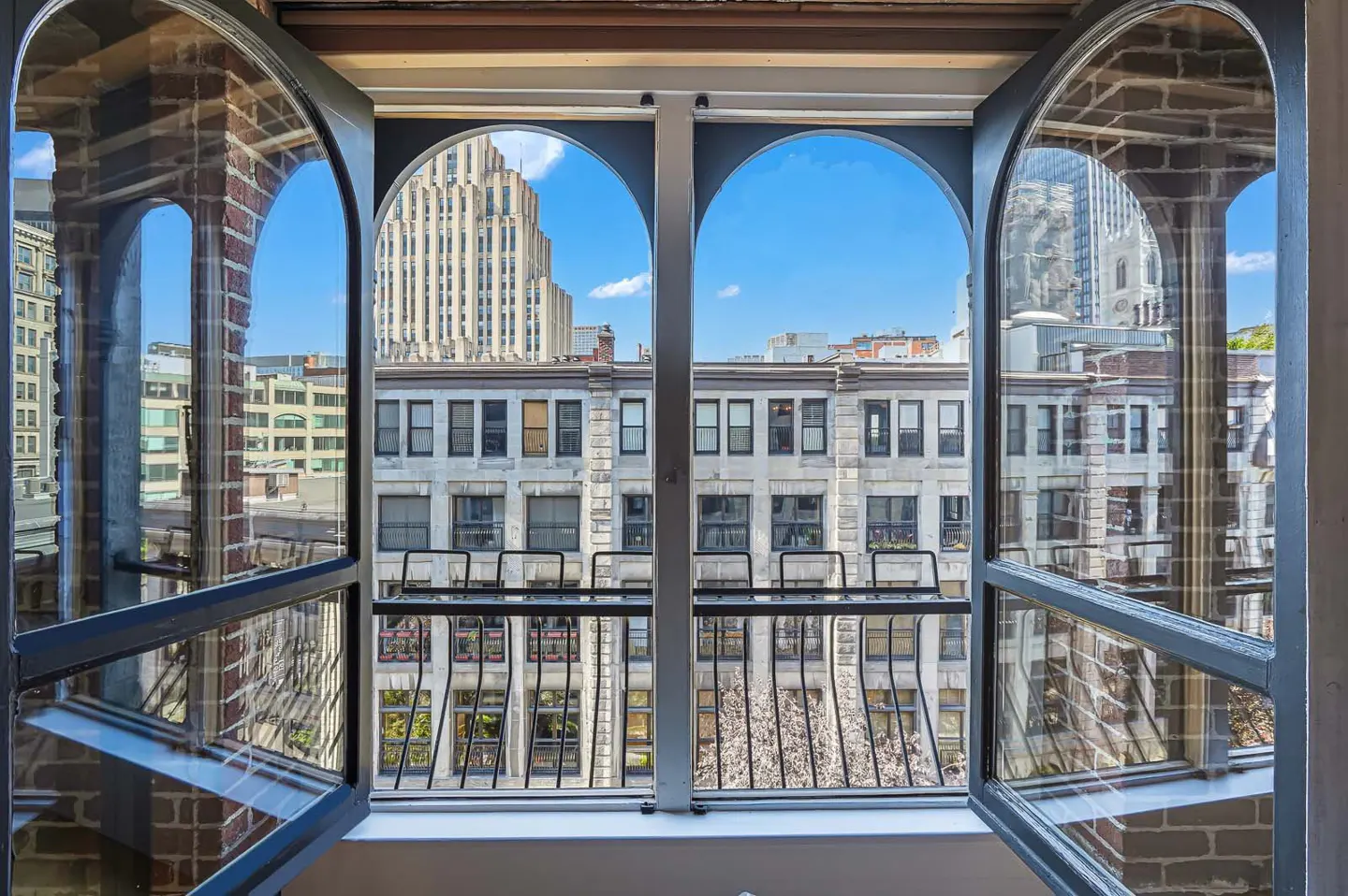 Open arched window with black frame, brick surround, and a view of city buildings under a blue sky.