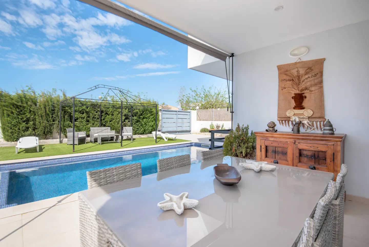Outdoor patio with a pool. A table with chairs is in the foreground. A gazebo and lawn furniture are by the pool.