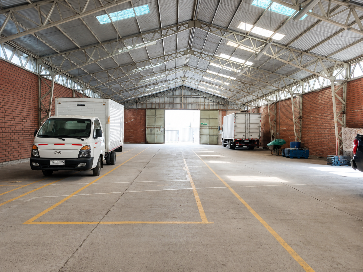 Spacious warehouse with brick walls, metal truss ceiling, concrete floor with yellow markings, and two parked box trucks. [AI-generated text]