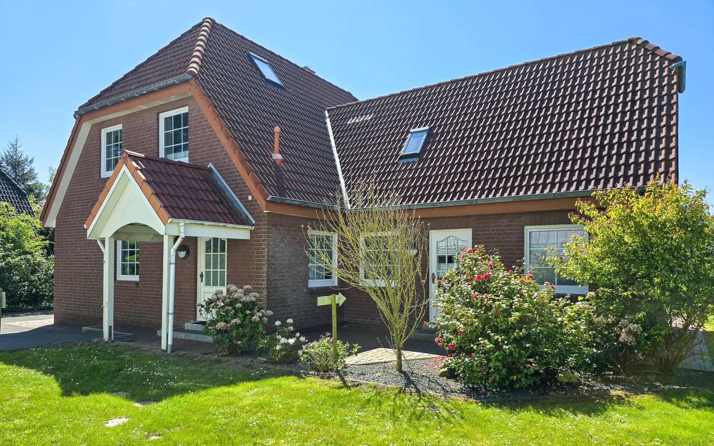 Two-story brick house with a brown tiled roof, white trim, and green lawn on a sunny day.