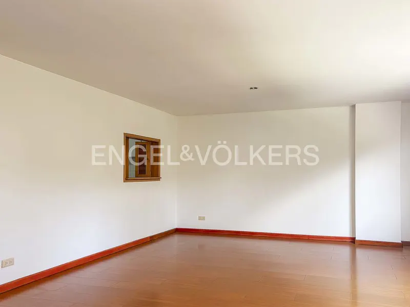 Empty room with hardwood floors, white walls, and a wood-framed window. Engel & Völkers logo is superimposed on the wall.