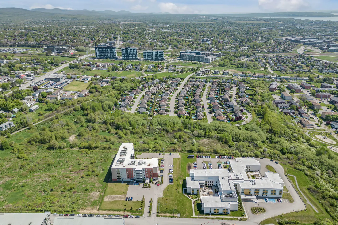 Aerial view of a suburban neighborhood with apartment buildings, residential streets, and green spaces under a blue sky.