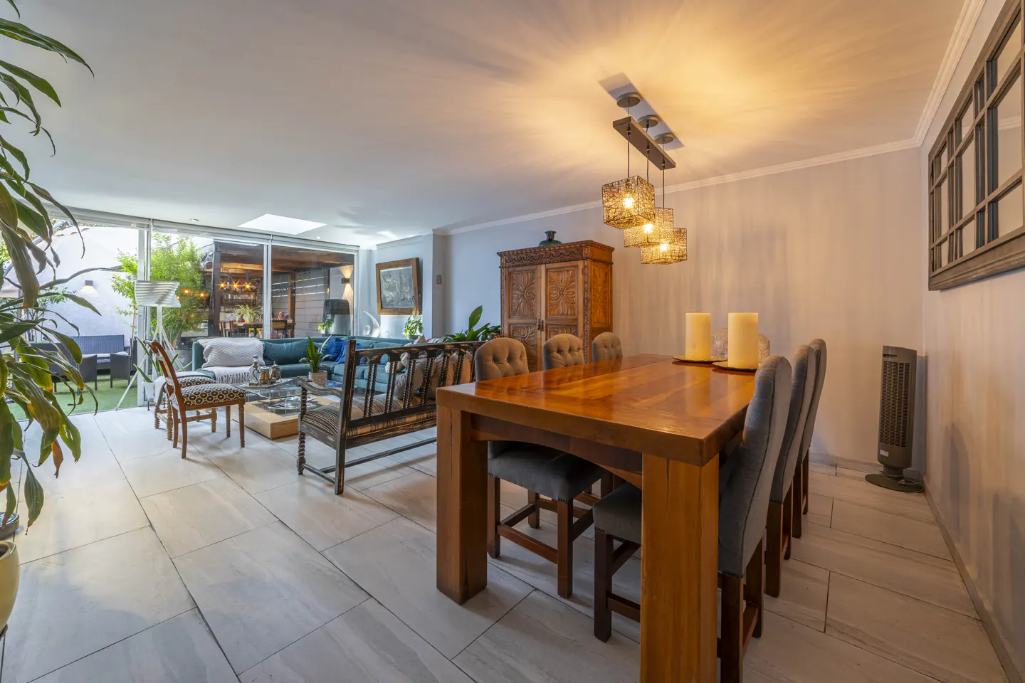 Open-concept living and dining area with a wooden table, gray chairs, and a blue sofa. A cabinet and outdoor patio are visible.