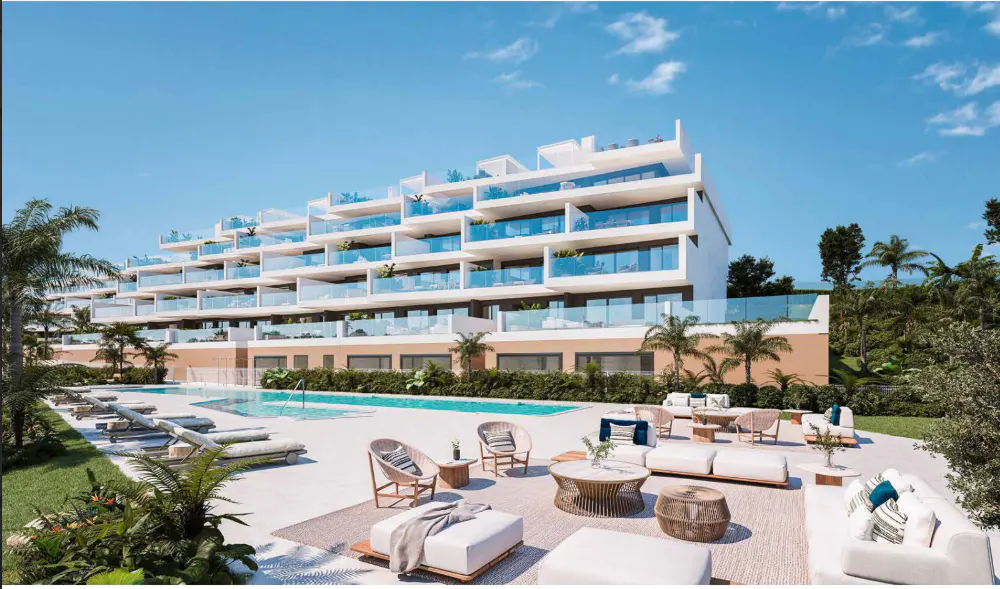 Modern white apartment building with blue glass balconies overlooks a pool and lounge area with white sofas and palm trees.