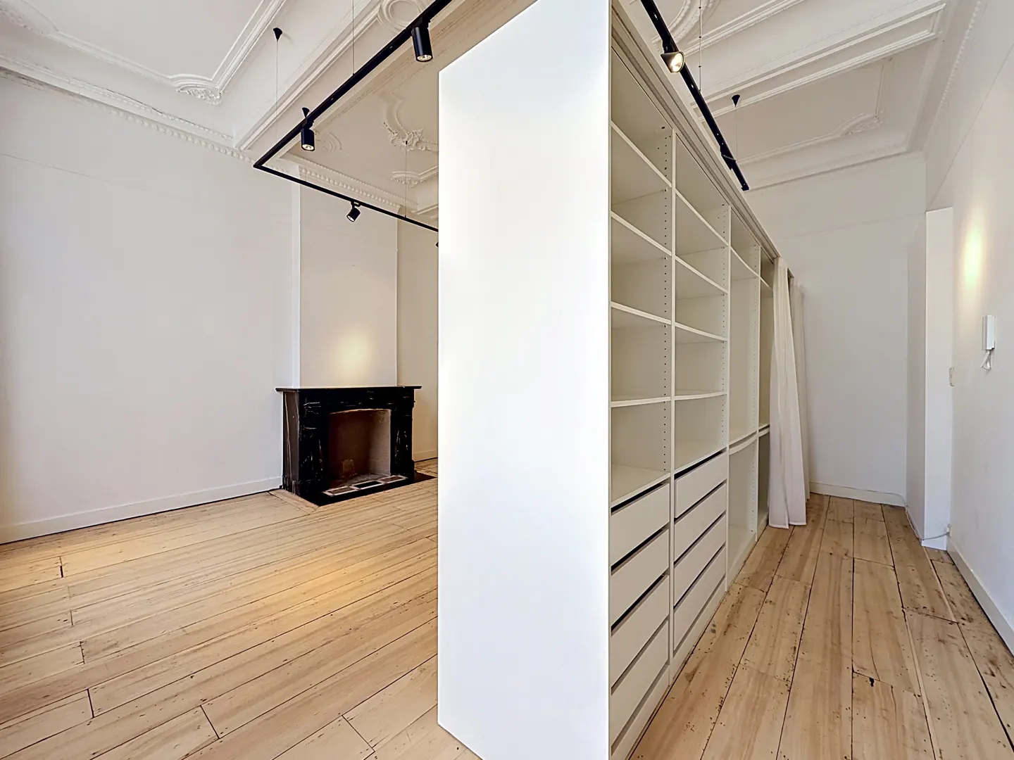 Modern room with light wood floors, a white walk-in closet partition, track lighting, and a black marble fireplace.