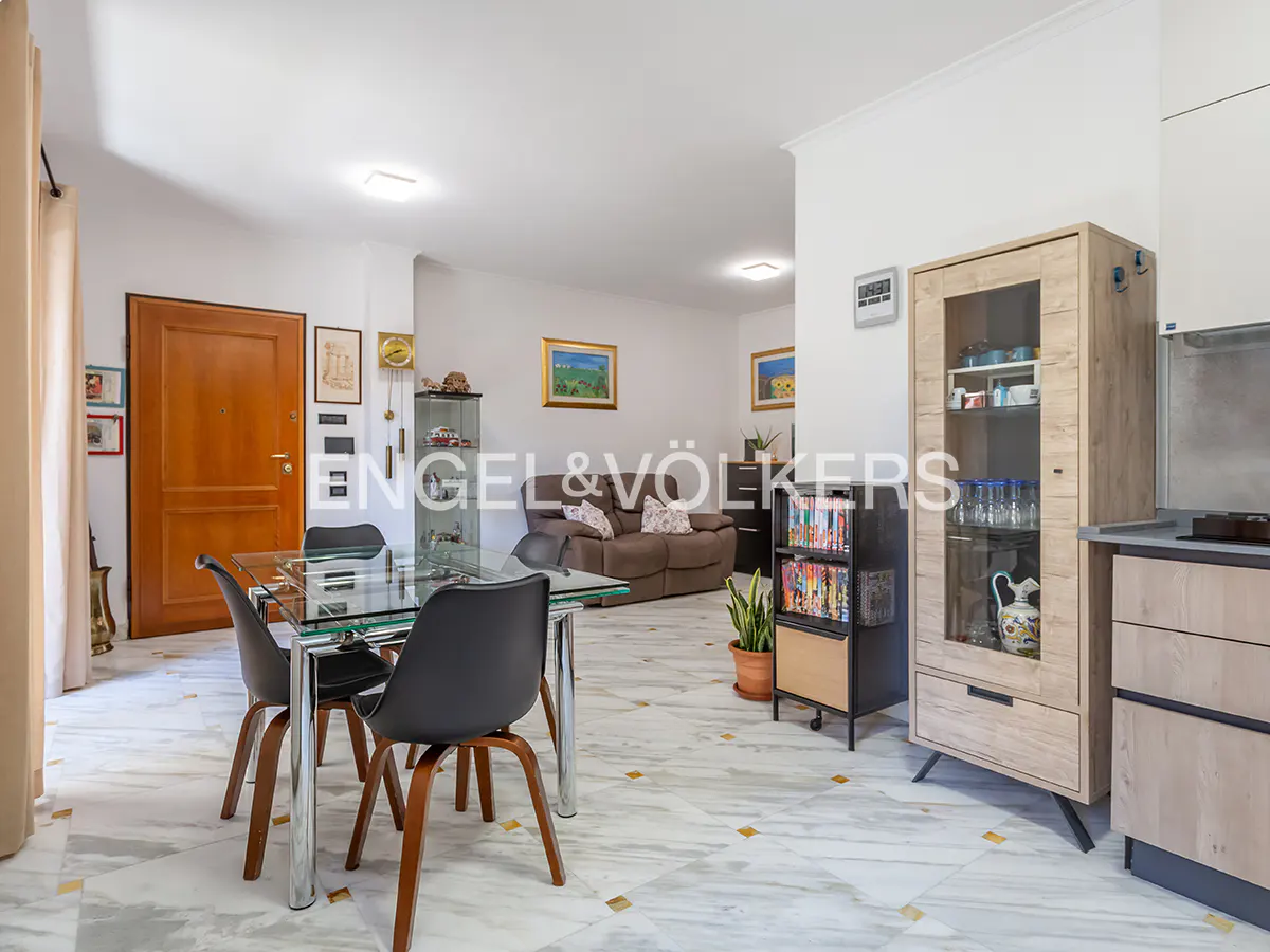 Open-plan living area with a glass dining table, black chairs, marble floors, a brown sofa, and a light wood display cabinet.