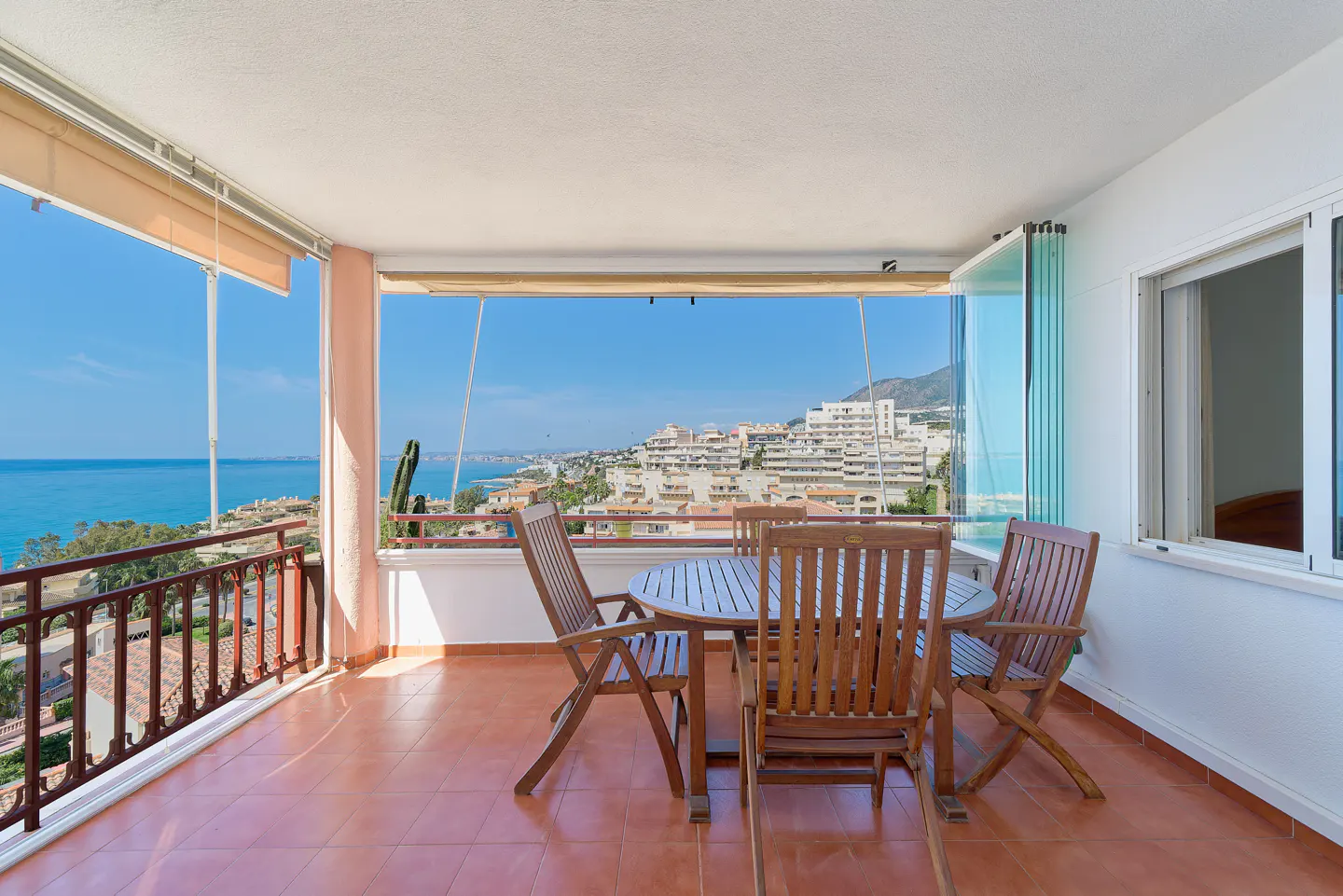 Balcony with a wooden table and chairs overlooking the ocean and city.