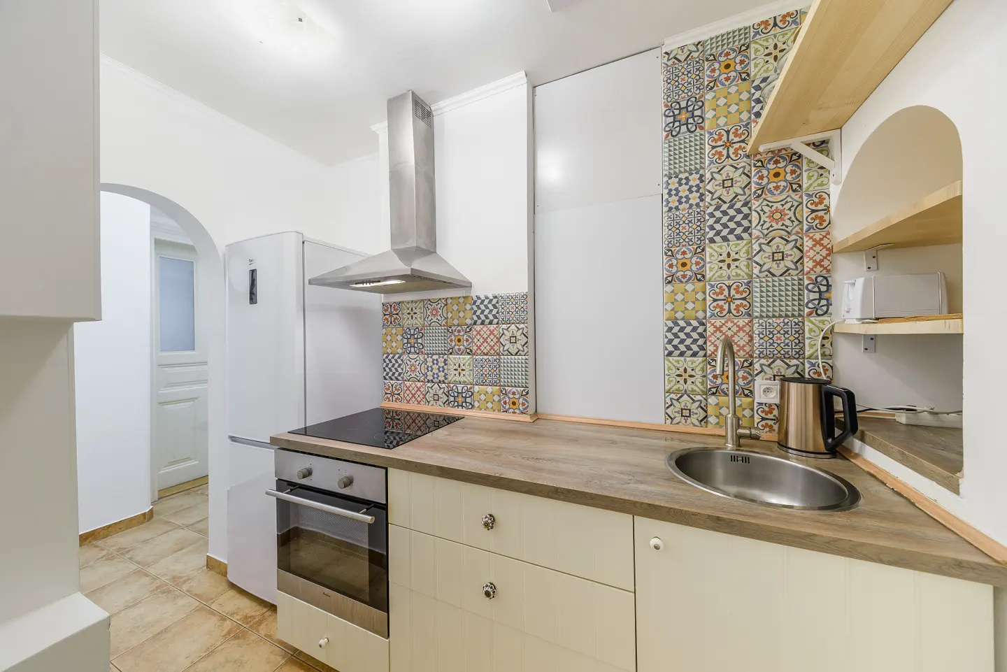 Modern kitchen with white cabinets, wood countertops, stainless steel appliances, and colorful patterned tile backsplash.