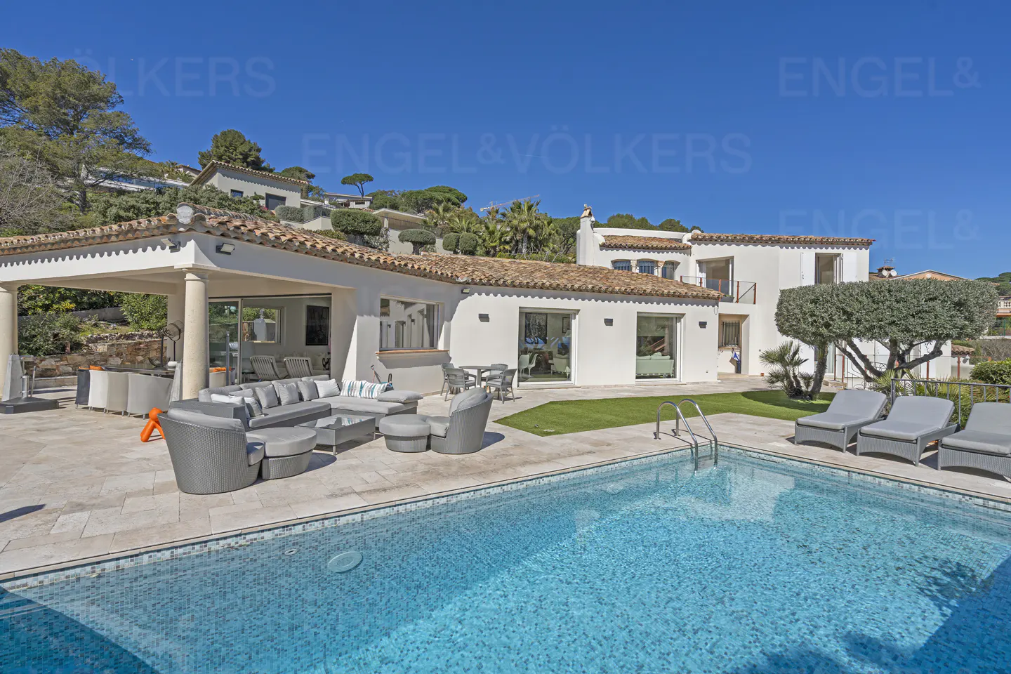 Exterior of a white villa with a pool, patio furniture, and a red tile roof under a clear blue sky.