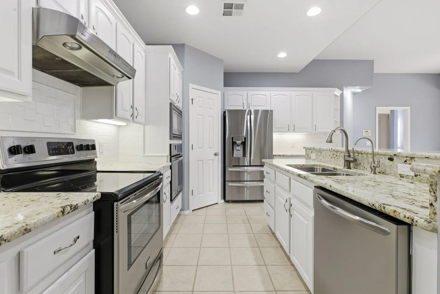 Bright kitchen with white cabinets, stainless steel appliances, and granite countertops. Tiled floor and gray walls.