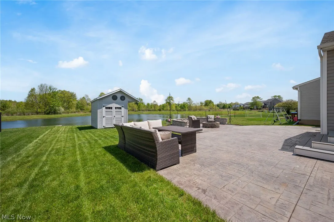 Backyard patio with wicker furniture, a shed, and a pond under a blue sky.