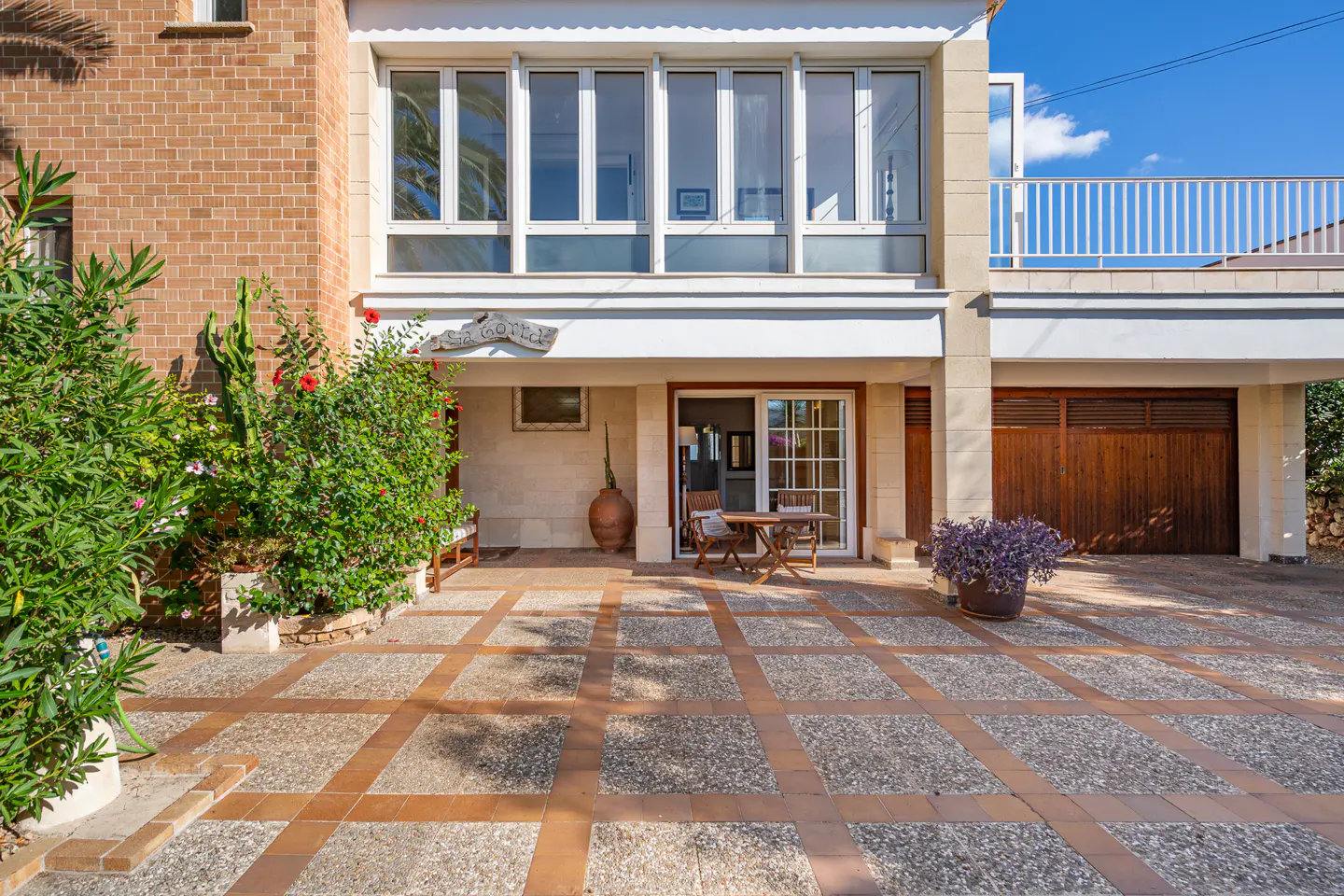 Two-story house with brick and stucco exterior, a patio with table and chairs, and a wooden garage door.