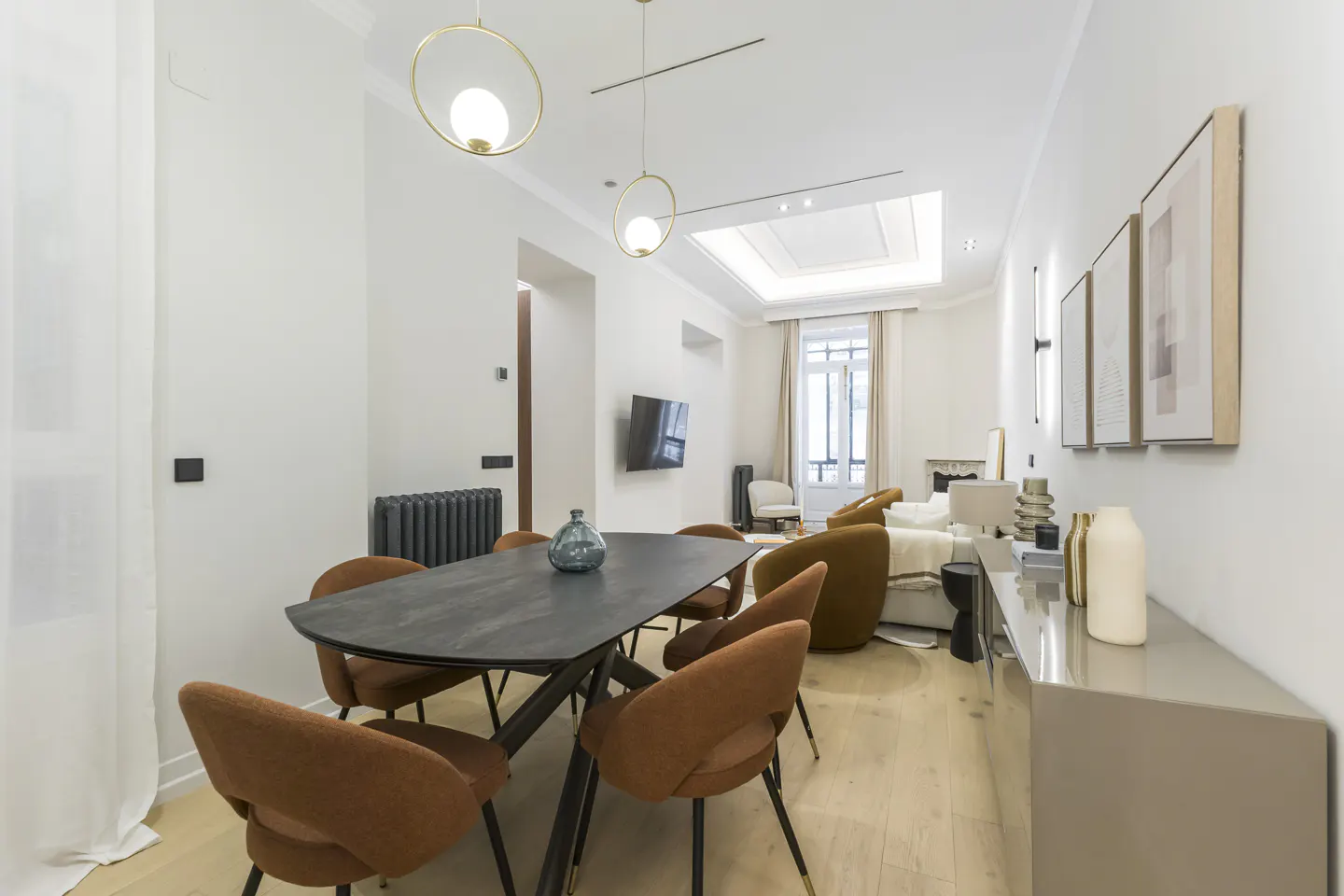 Modern dining room with a black table, rust-colored chairs, light wood floors, and gold pendant lights.