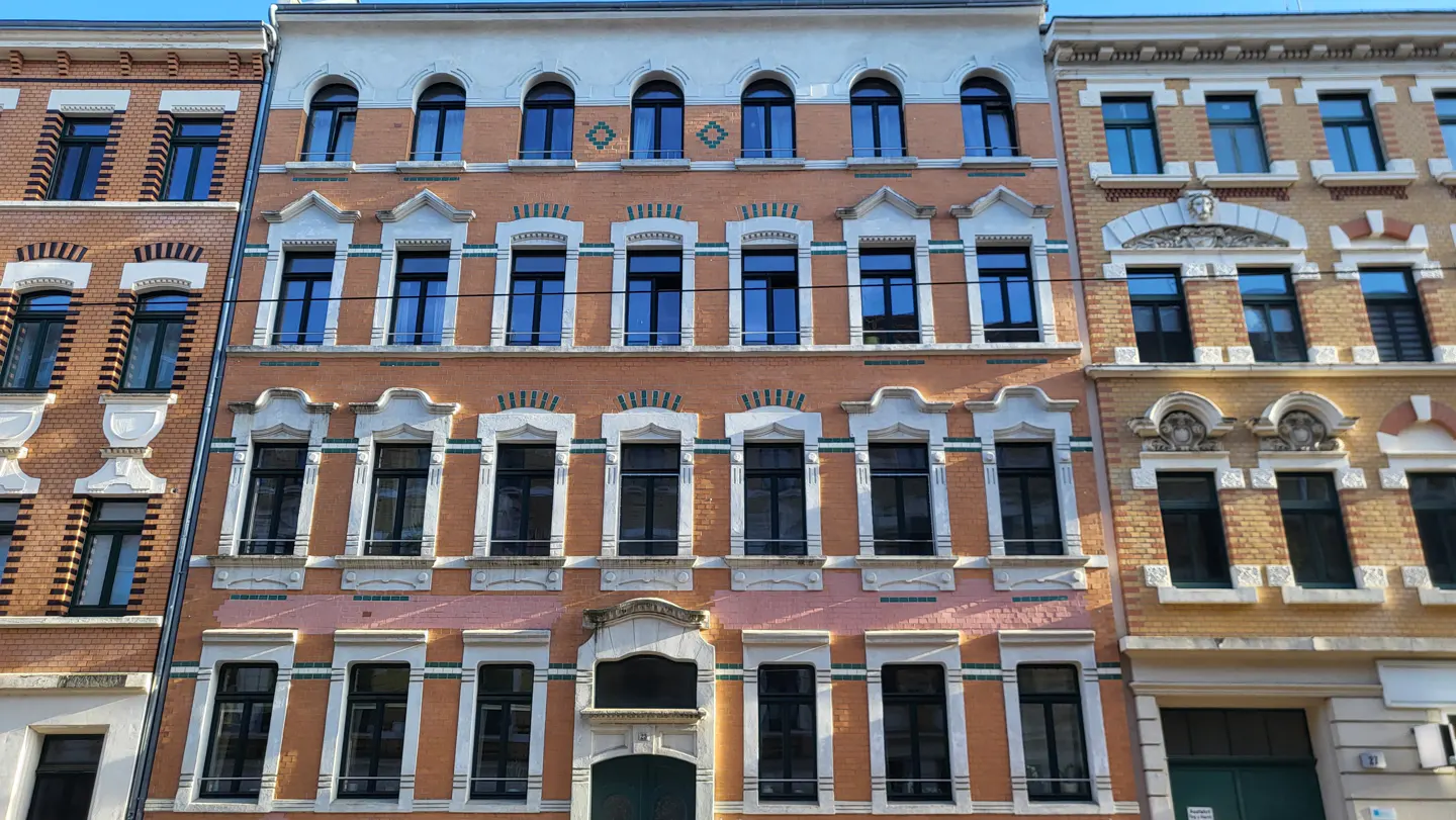 A four-story orange brick building with black-framed windows and a green door.