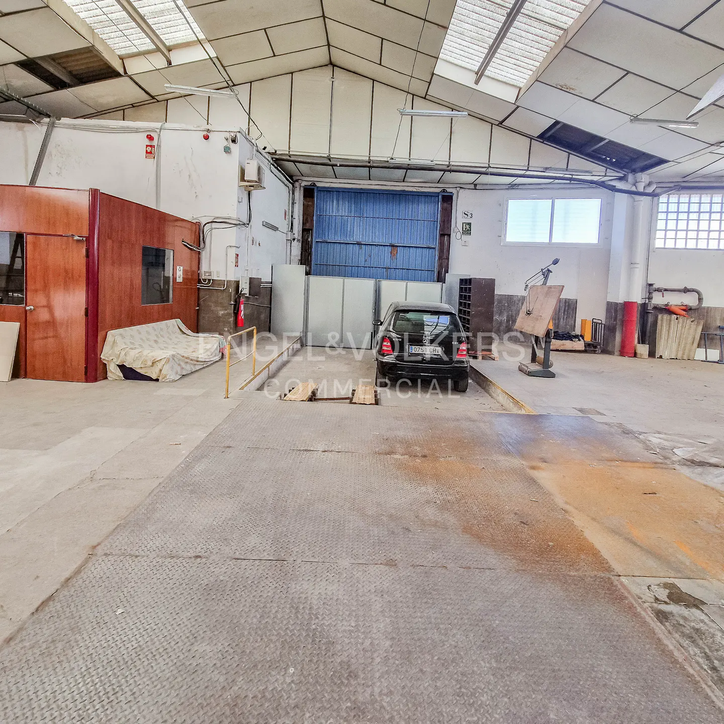 A spacious warehouse interior with a black car on a metal platform, under a high ceiling with skylights.