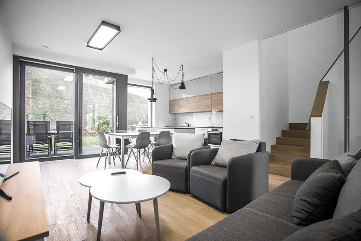 Modern open-plan living room with grey armchairs, a white coffee table, and a kitchen with wood-toned cabinets.