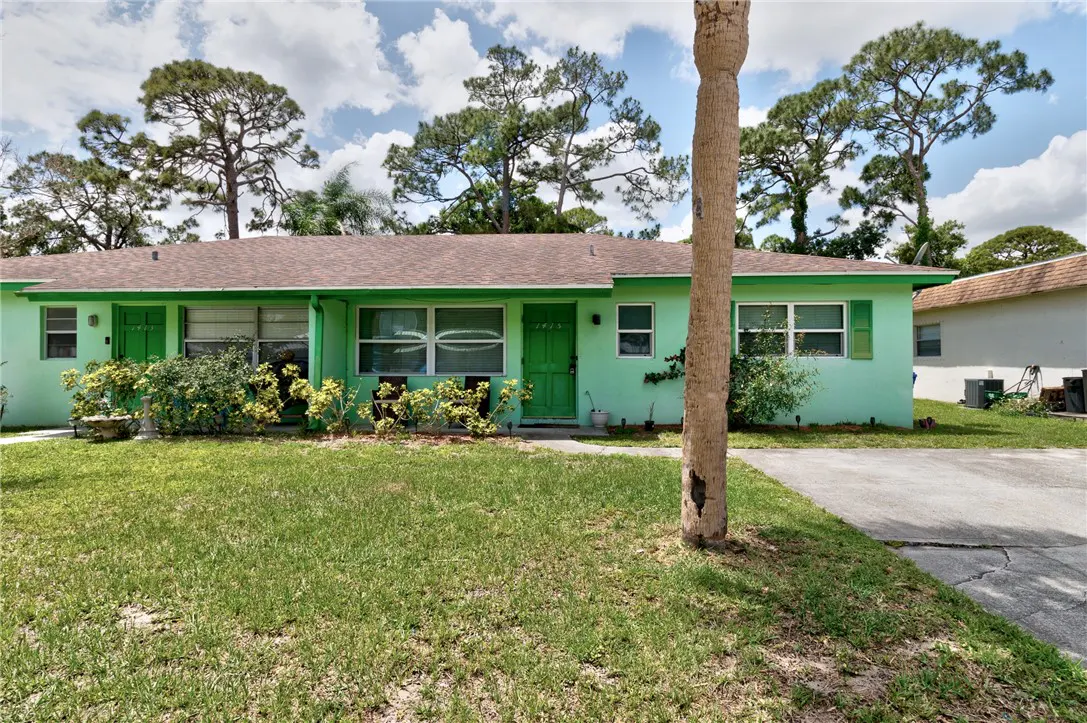 A light green duplex with a brown roof, green door, and green trim, surrounded by a green lawn and trees.