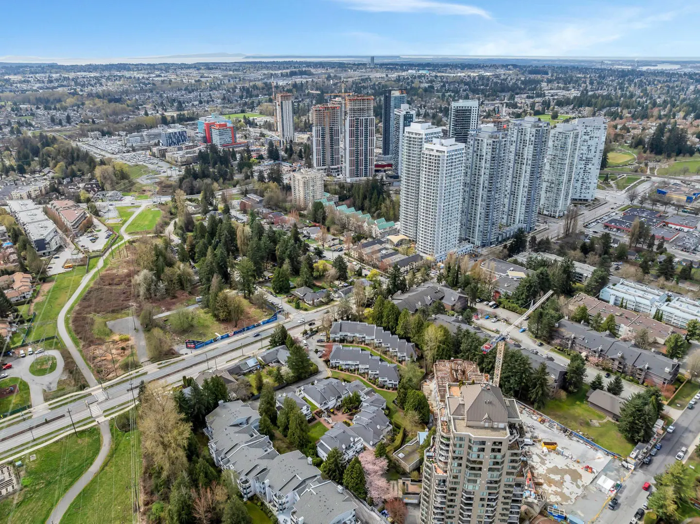 Aerial view of a city with high-rise buildings, townhouses, green spaces, and a blue sky.
