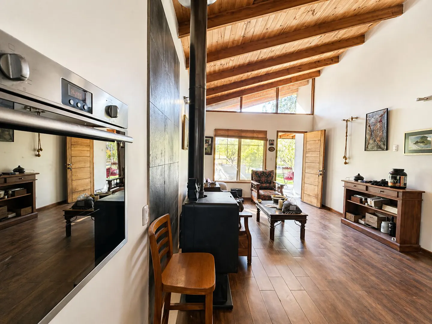Interior view of a living room with a wood-burning stove, wooden floors, and a vaulted ceiling with exposed beams.