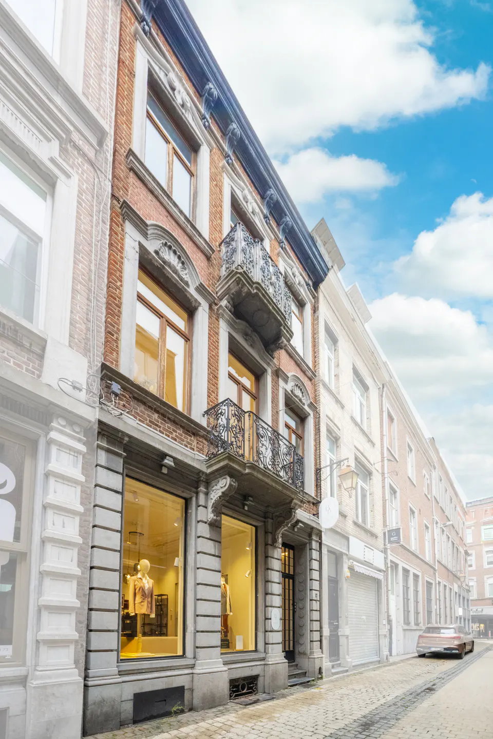 A three-story brick building with a black iron balcony on the second floor. Large windows are on the first floor.