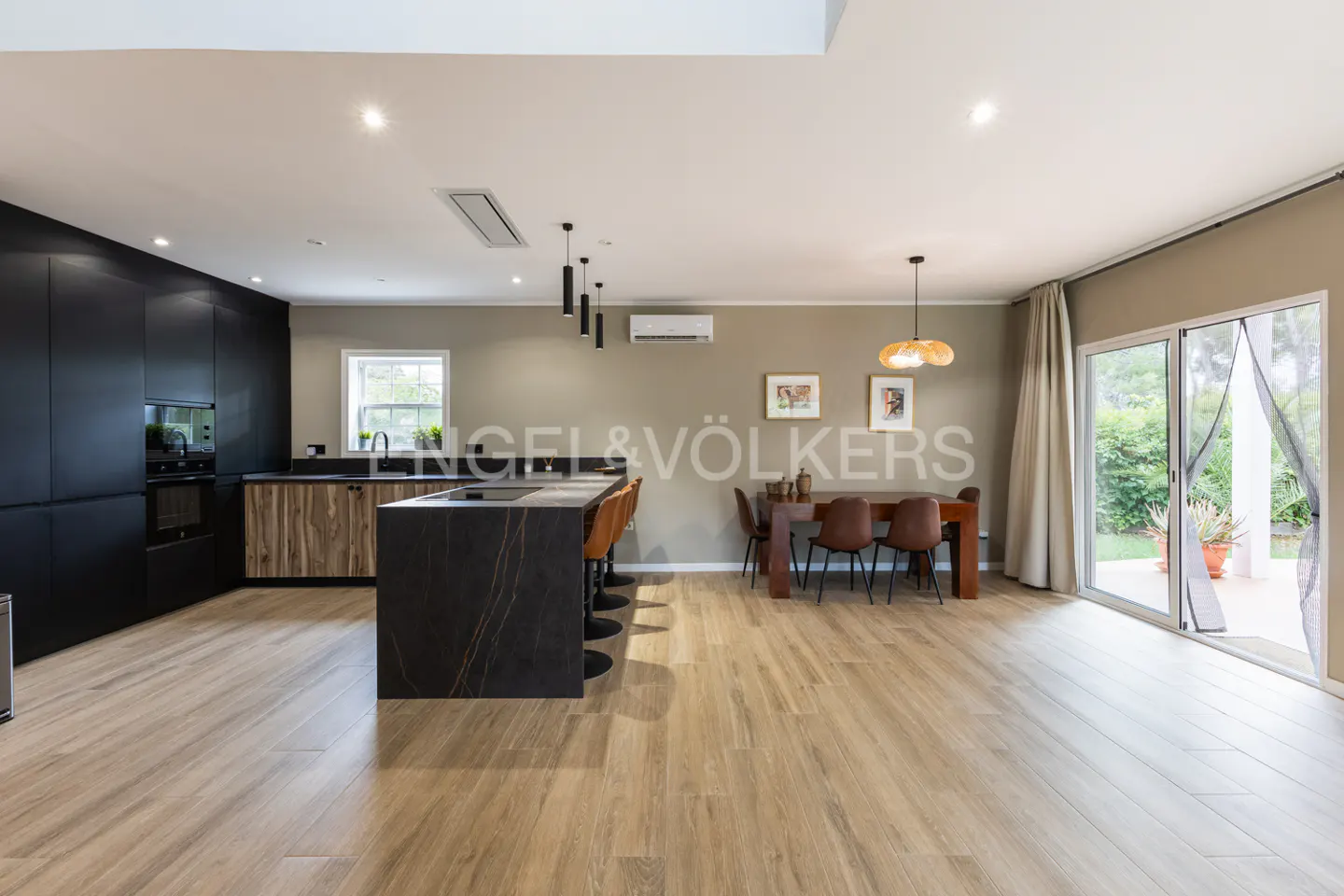 Open-concept kitchen and dining area with black cabinets, island, wood table, and sliding glass doors to the outside.