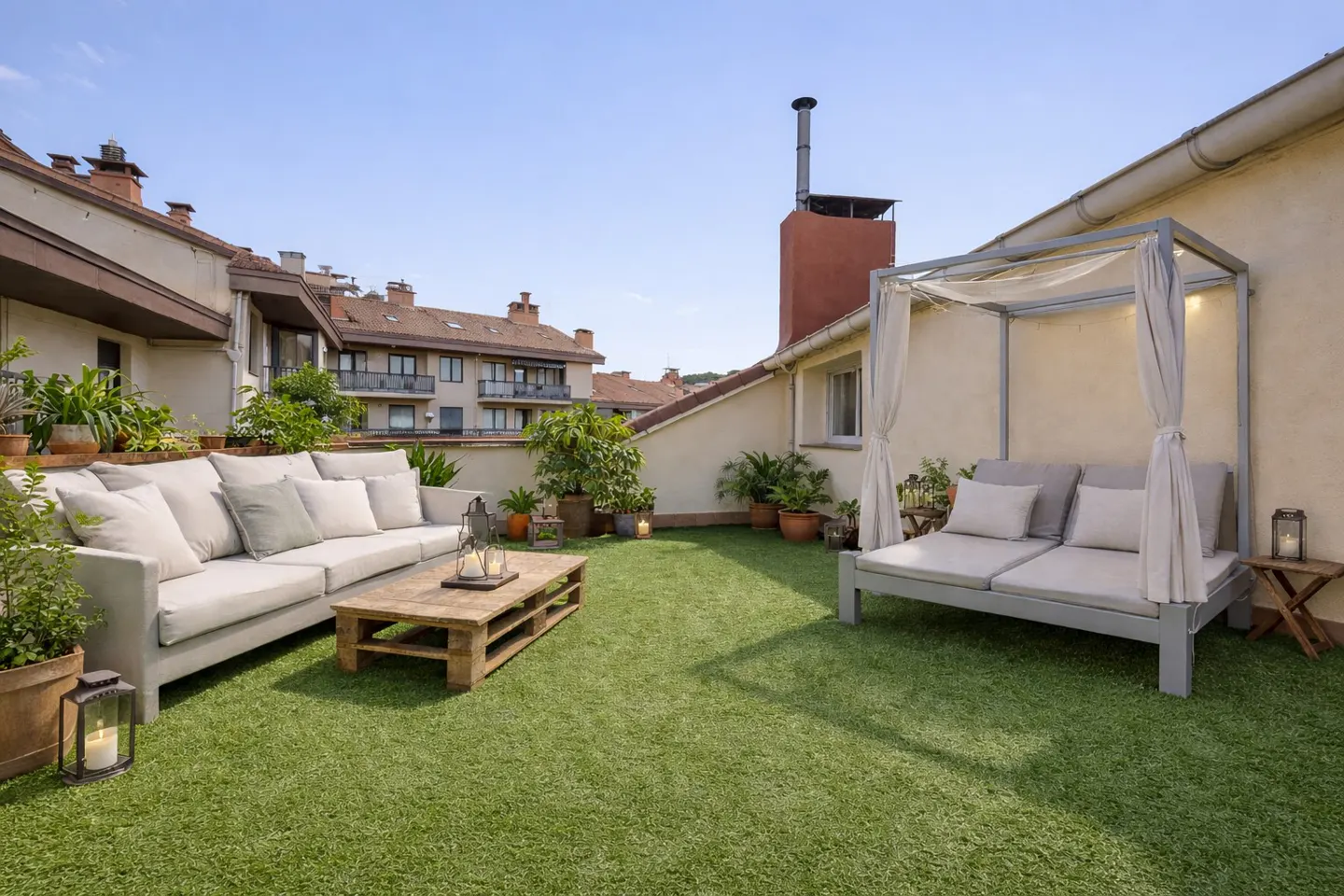 Rooftop patio with green turf, a gray sofa, a pallet coffee table, and a daybed with a canopy. Potted plants add greenery.