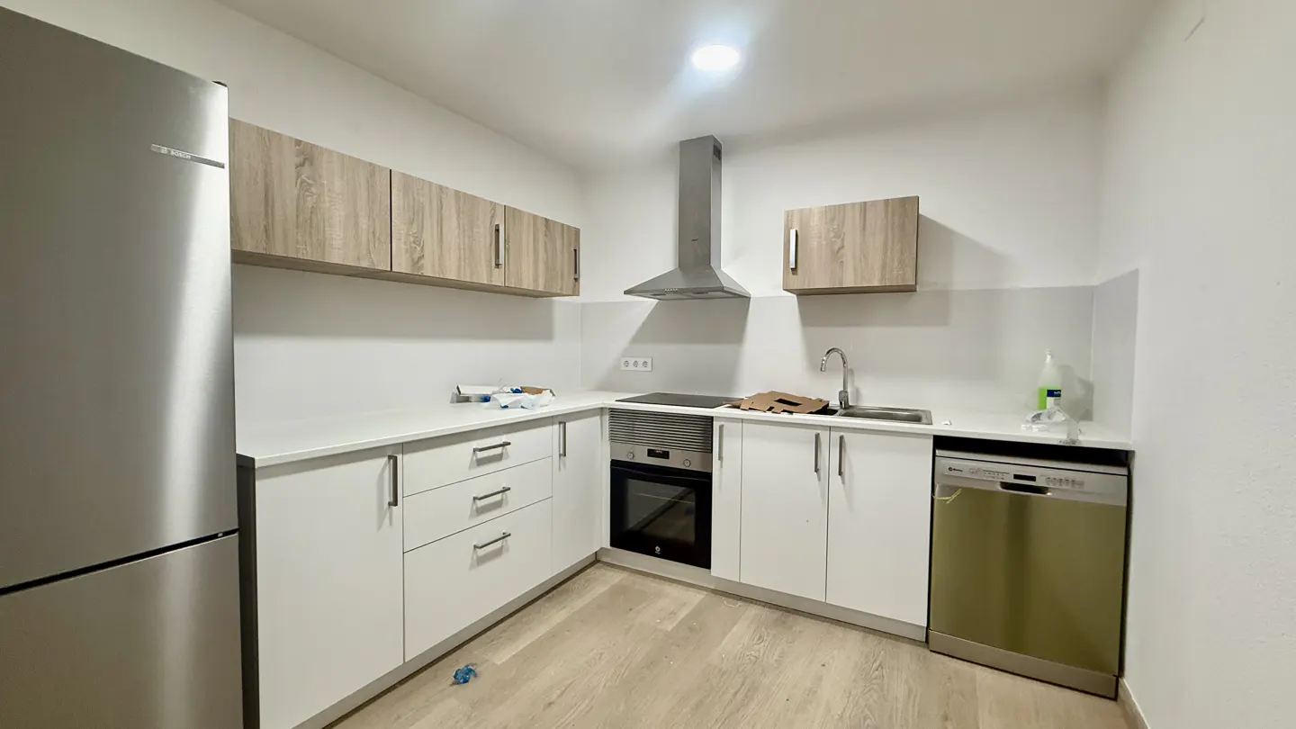 A bright kitchen with white cabinets, light wood accents, stainless steel appliances, and light wood flooring.