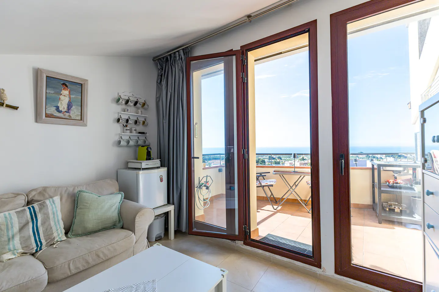 Living room with beige sofa, mini fridge, and open doors to a balcony with ocean view.