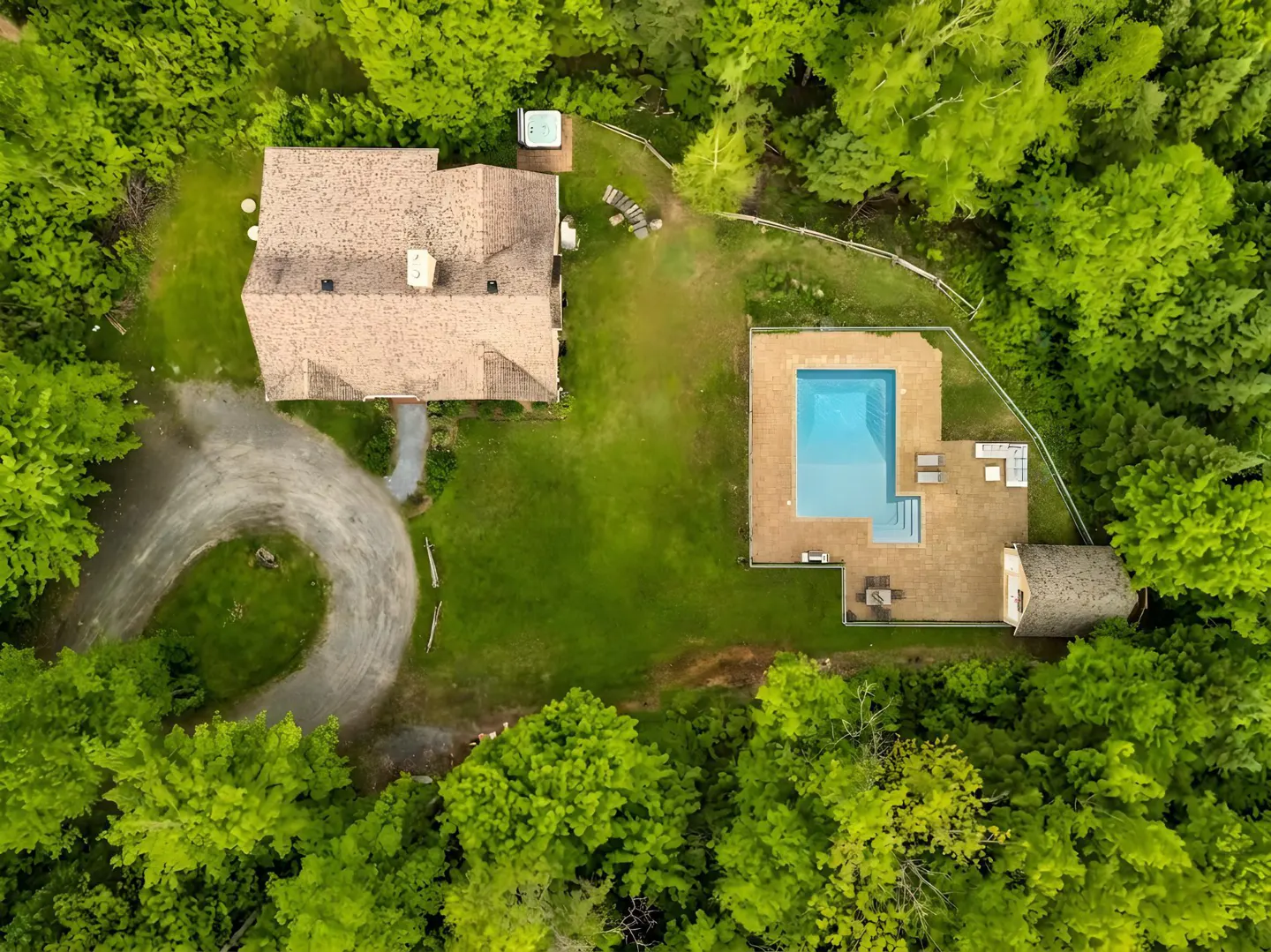 Aerial view of a house with a circular driveway, a swimming pool, and a patio, surrounded by dense green forest.