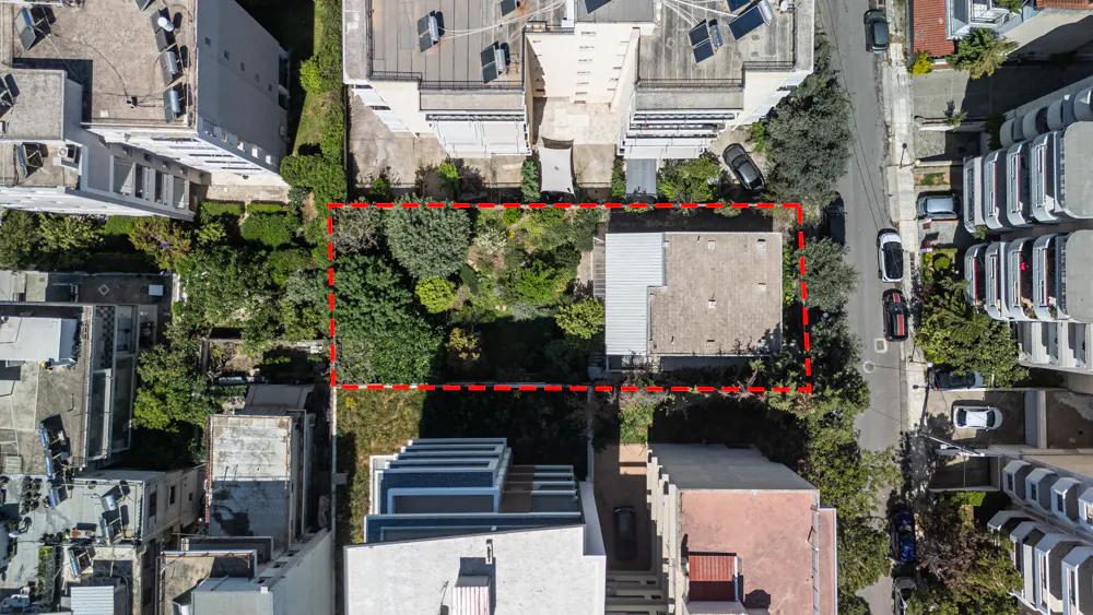 Aerial view of a property outlined in red, featuring a house, lush greenery, and surrounding buildings.