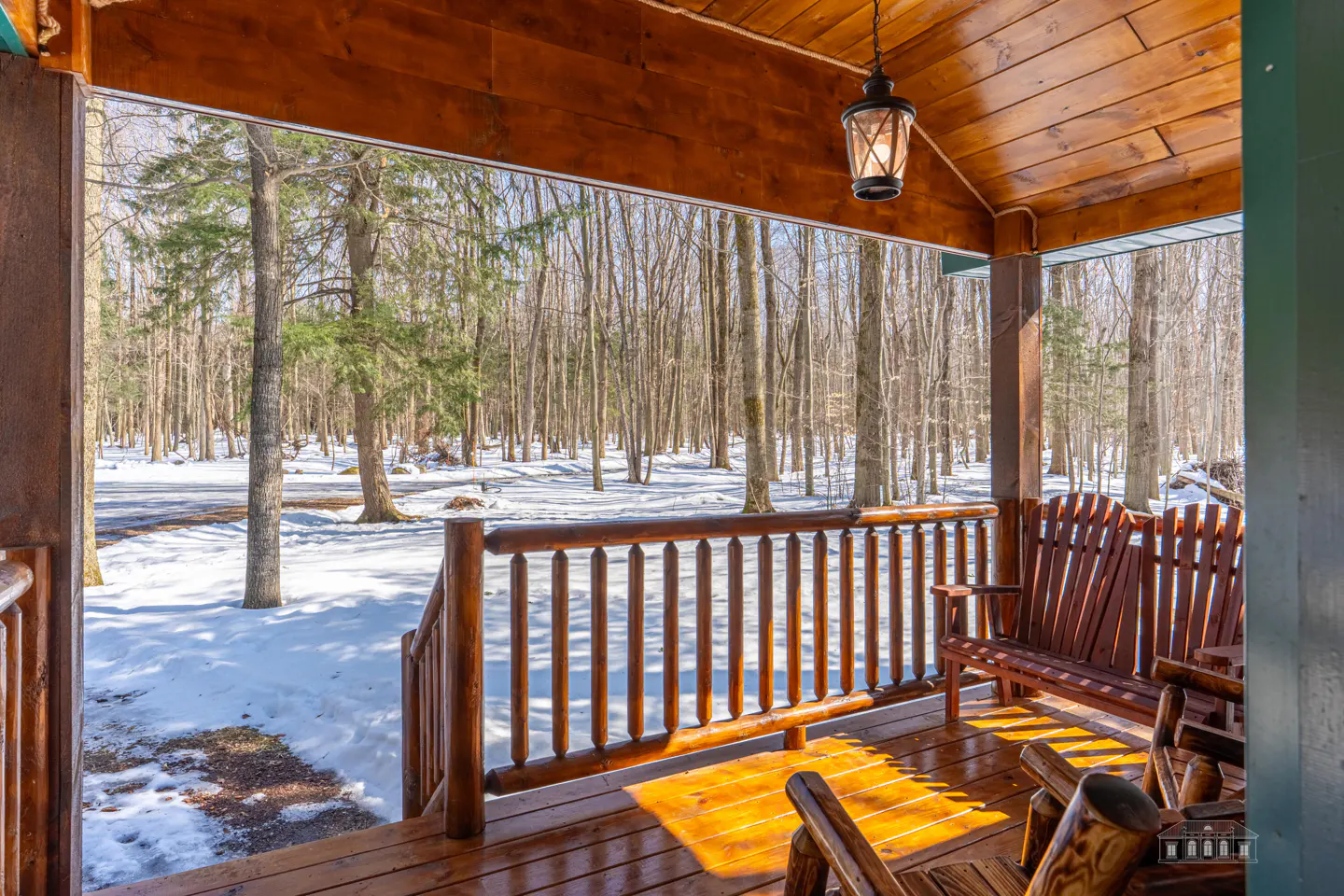 View from a wooden porch with chairs, overlooking a snowy forest.