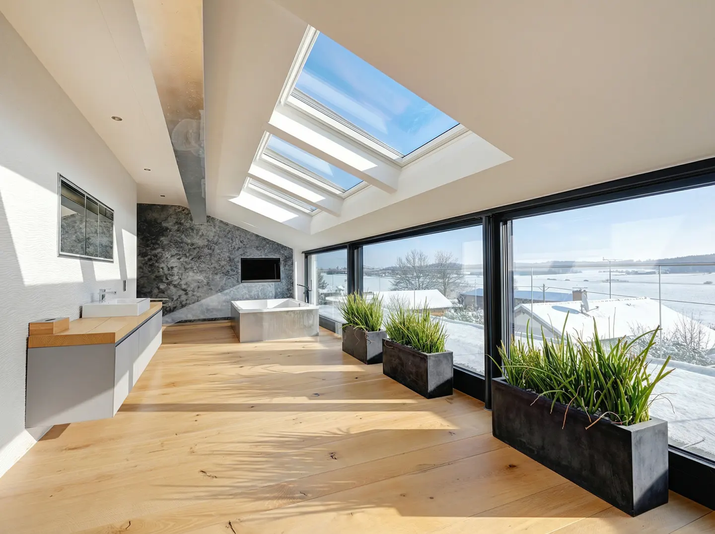 Modern bathroom with light wood floors, skylights, a soaking tub, and large windows overlooking a snowy landscape.