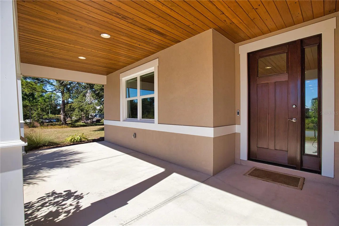Covered porch with a brown front door, white trim, and a wood plank ceiling. A window is on the left side of the door.