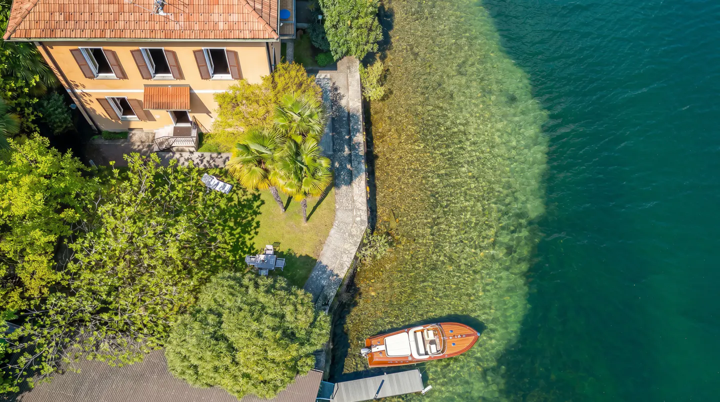 Aerial view of a yellow house with brown shutters next to a lake with a boat docked.