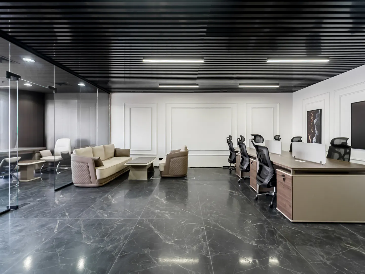 Office space with black marble floors, a black slatted ceiling, and white walls. A beige sofa and chairs sit near a glass-walled conference room. Desks and chairs line the opposite wall.