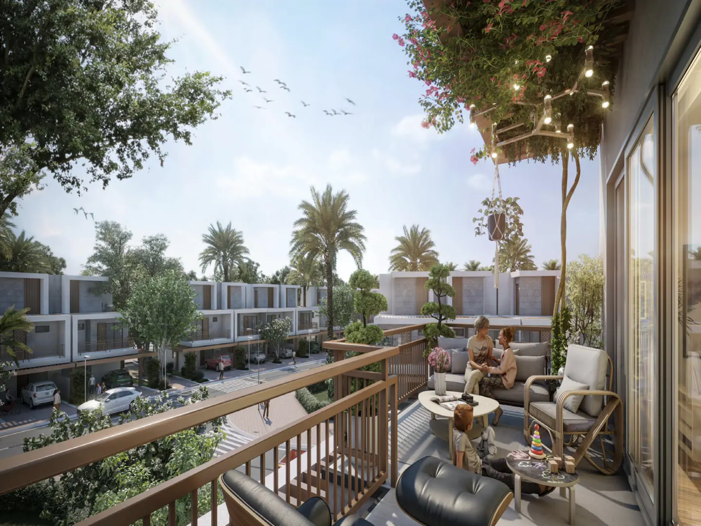Balcony view of modern townhouses. Family relaxes on outdoor furniture. Lush greenery, palm trees, and blue sky with birds in the background.
