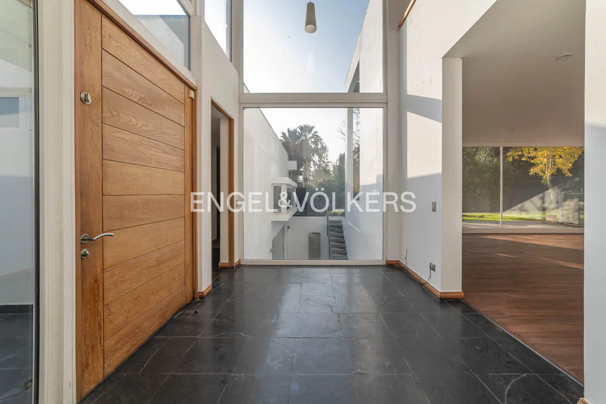 Modern home foyer with a wood door, black tile floor, and large windows showing a courtyard.