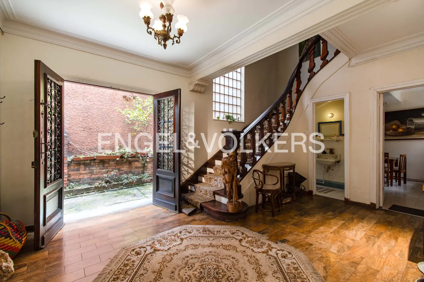 A foyer with an open door to a courtyard, a staircase, and a chandelier.
