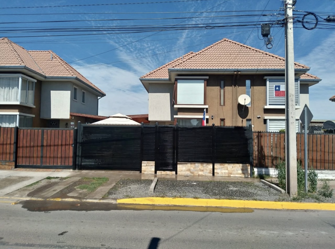 Two-story houses with brown roofs and fences, one with a Chilean flag, under a blue sky.