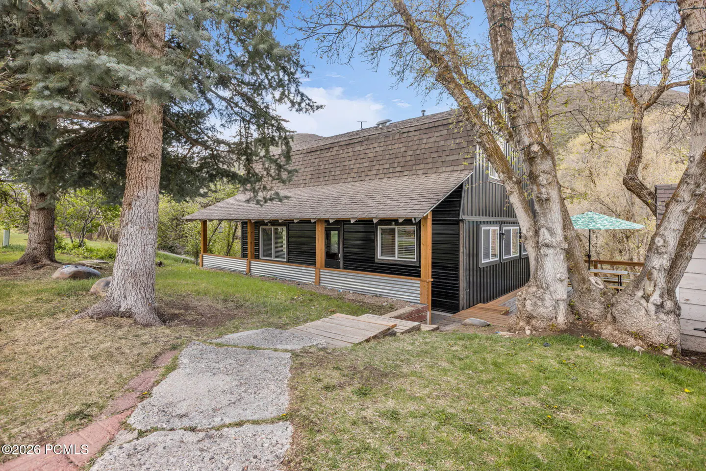 A black house with a brown roof and a porch, surrounded by trees and green grass.